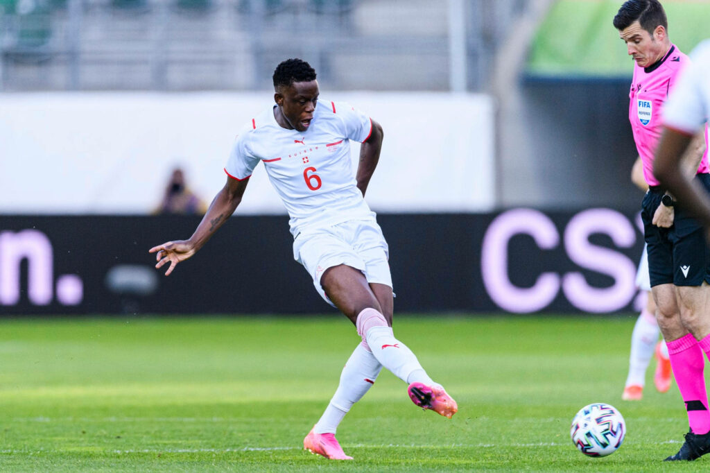 Denis Zakaria kicking football in white Swiss kit number 6 on green field during intense match Wallpaper