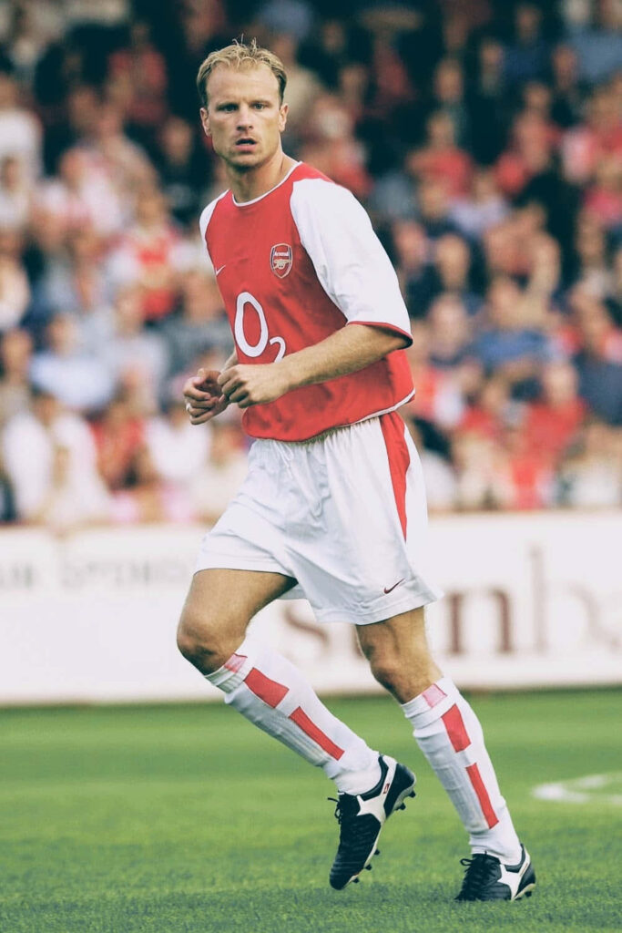 Dennis Bergkamp in classic Arsenal kit skillfully playing football on lush green pitch against Stevenage Wallpaper