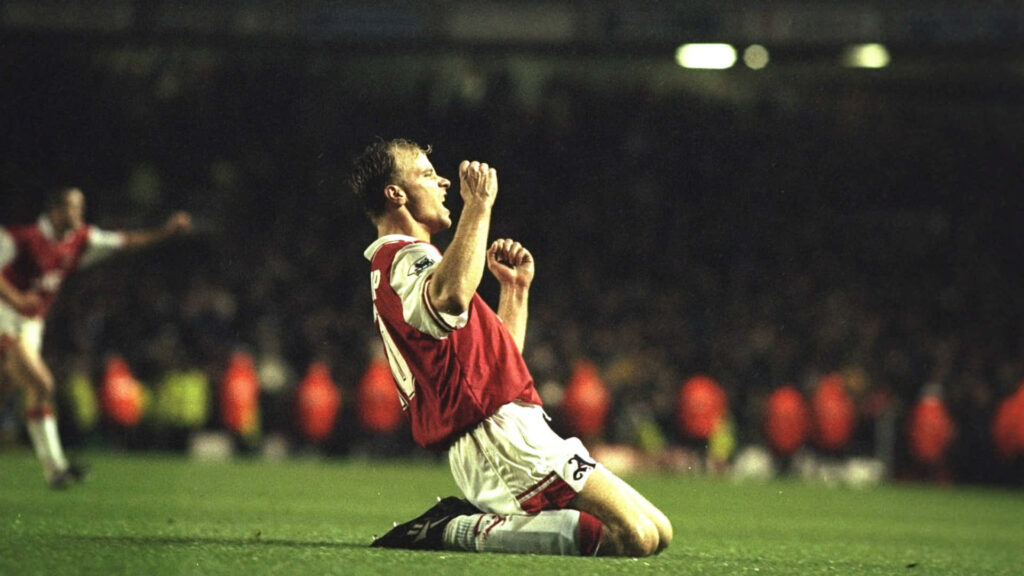 Dennis Bergkamp kneeling celebrating Arsenal victory over Tottenham Hotspur with stadium lights Wallpaper