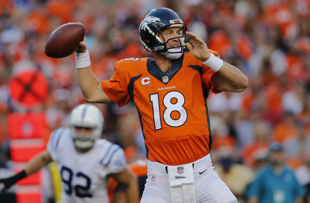 Denver Broncos player in orange and navy poised to throw football with blurred stadium fans Wallpaper