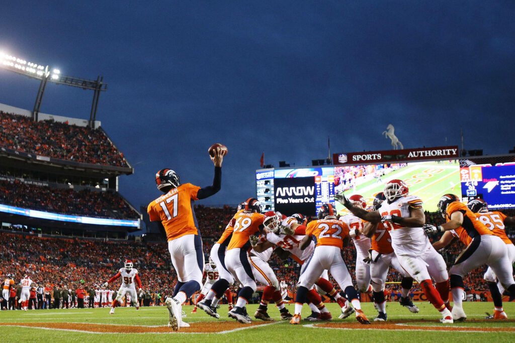 Denver Broncos NFL players in orange uniforms playing intense game in vibrant stadium at dusk Wallpaper