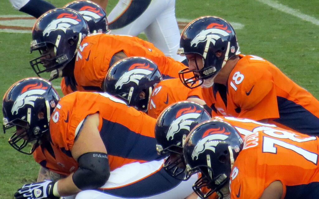 Denver Broncos football players in orange navy uniforms lined up ready stance on field wallpaper