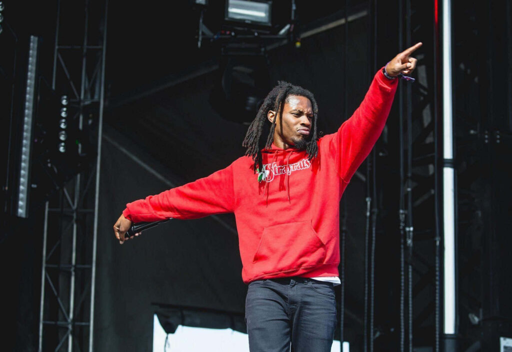 Denzel Curry live performance in red hoodie vibrant stage lighting urban concert atmosphere Wallpaper