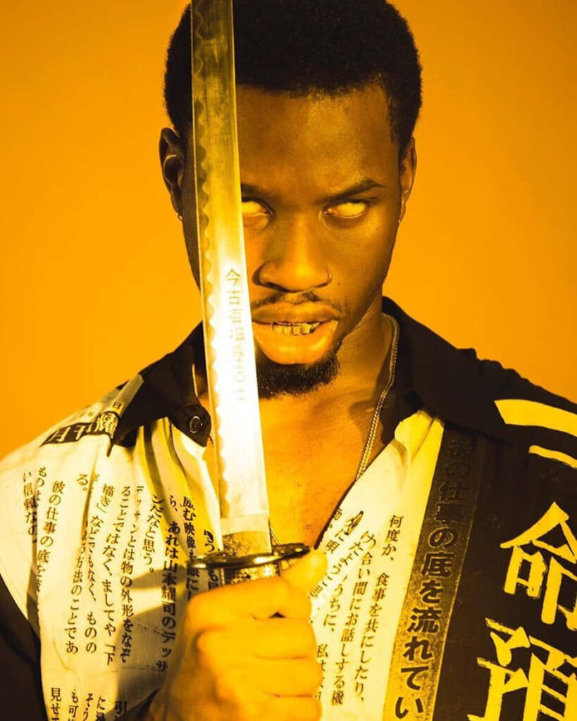 Denzel Curry intense gaze holding sword yellow background bold Japanese text edgy wallpaper