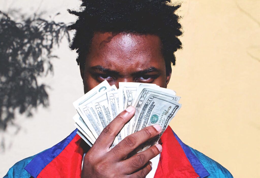 Denzel Curry holding cash fan with intense gaze vibrant jacket urban wallpaper background