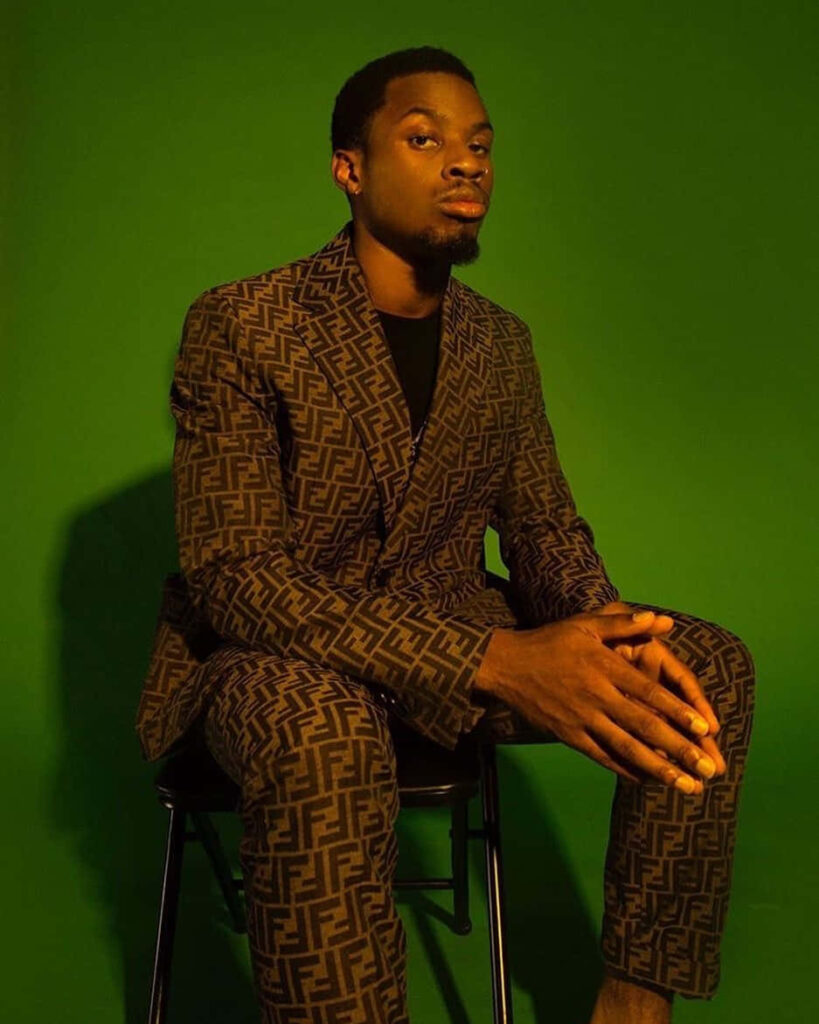 Denzel Curry in bold patterned brown designer suit on vibrant green backdrop stylish fashion portrait Wallpaper