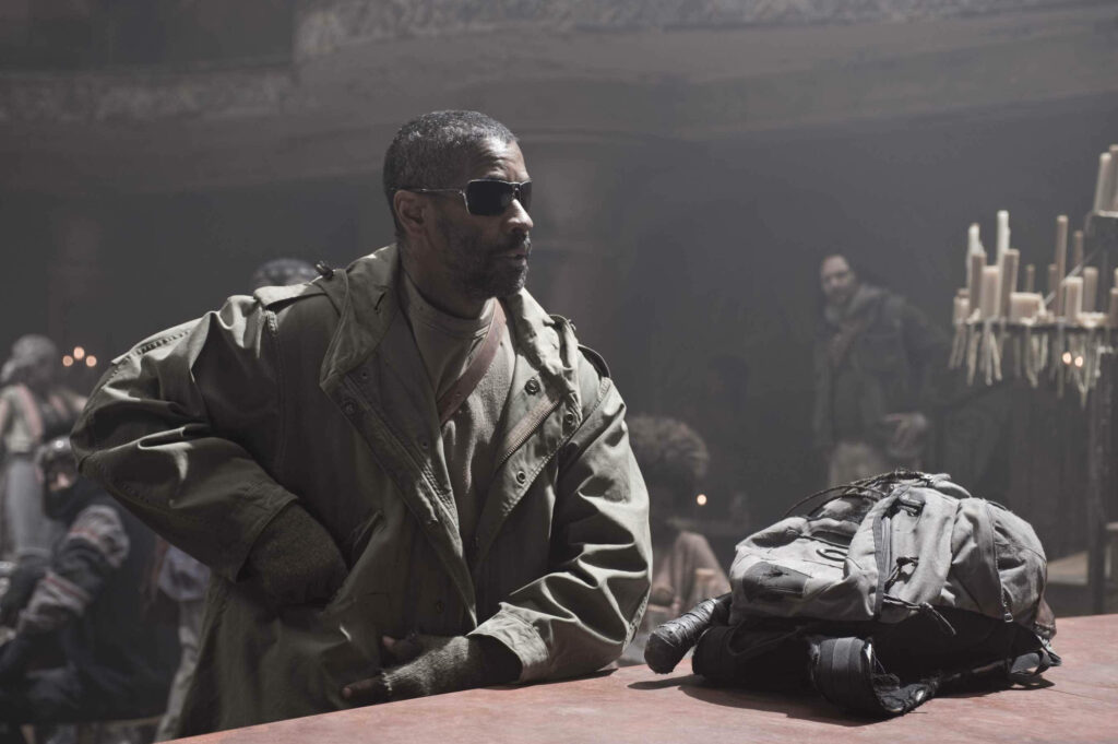 Denzel Washington in sunglasses and rugged coat leaning on table with backpack cool confident pose Wallpaper