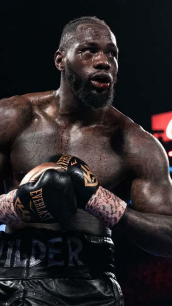 Deontay Wilder intense heavyweight boxing match action showing muscular focus and arena lighting Wallpaper