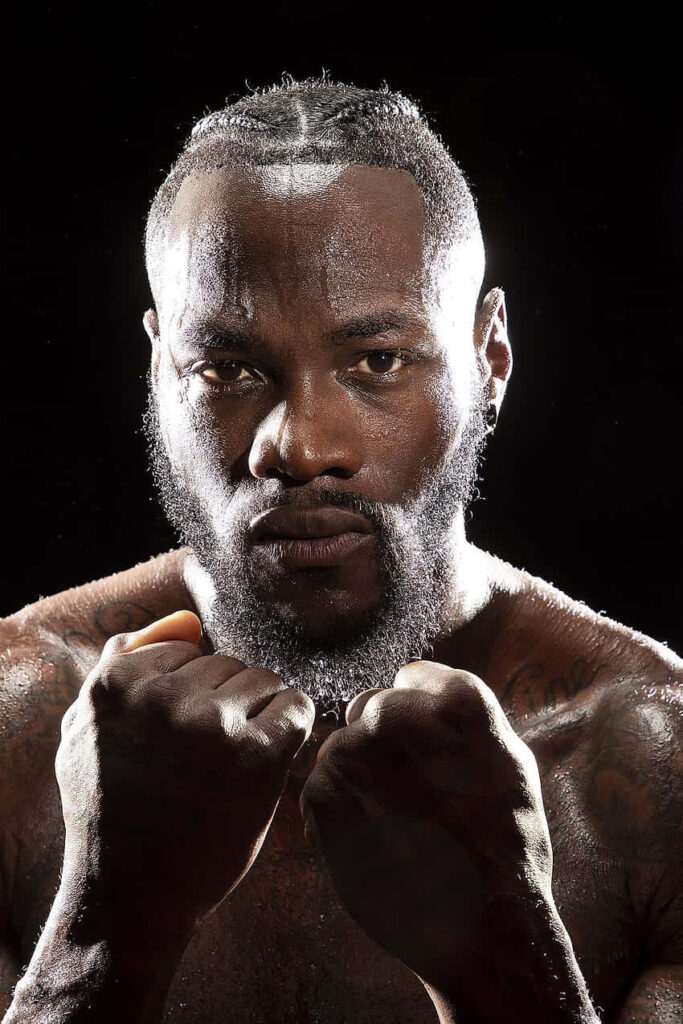 Deontay Wilder in classic boxing stance with intense gaze and muscular physique in dramatic light Wallpaper