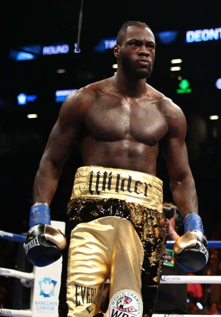Deontay Wilder boxing intense focus powerful physique gold black trunks vibrant arena lighting wallpaper