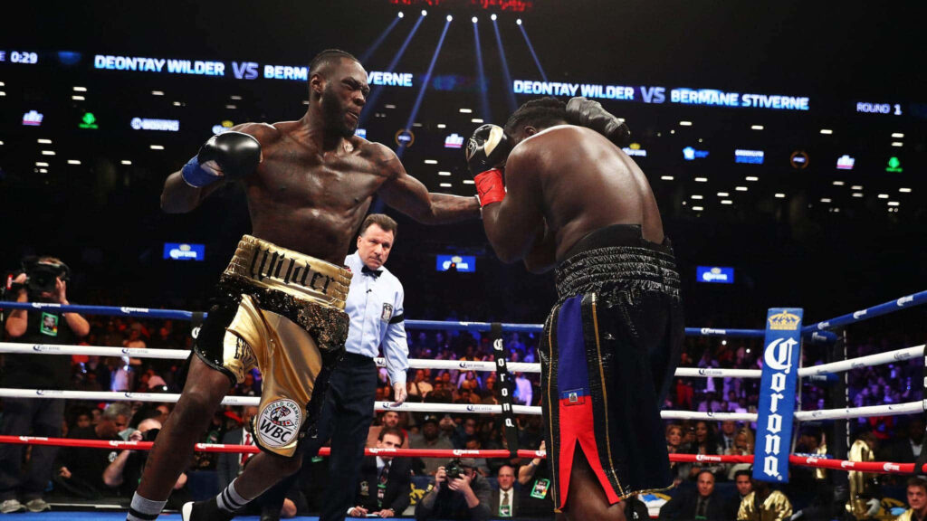 Deontay Wilder delivering a powerful punch in vibrant boxing ring during intense match action Wallpaper