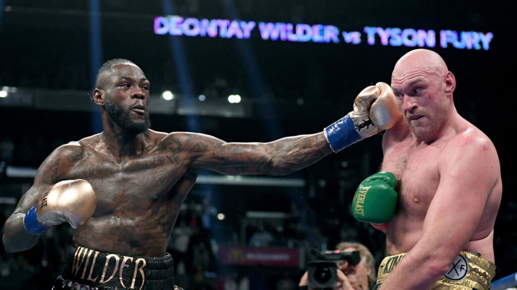 Deontay Wilder and Tyson Fury boxing mid-fight in ring with dramatic lighting and purple banner Wallpaper