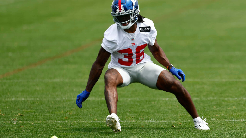 Deonte Banks in Giants gear mid-drill on green football field showing focus and agility Wallpaper
