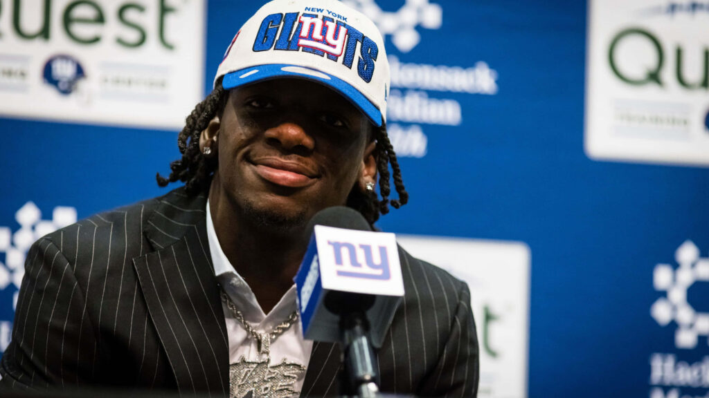 Deonte Banks in New York Giants cap and pinstripe suit at official team press conference backdrop Wallpaper