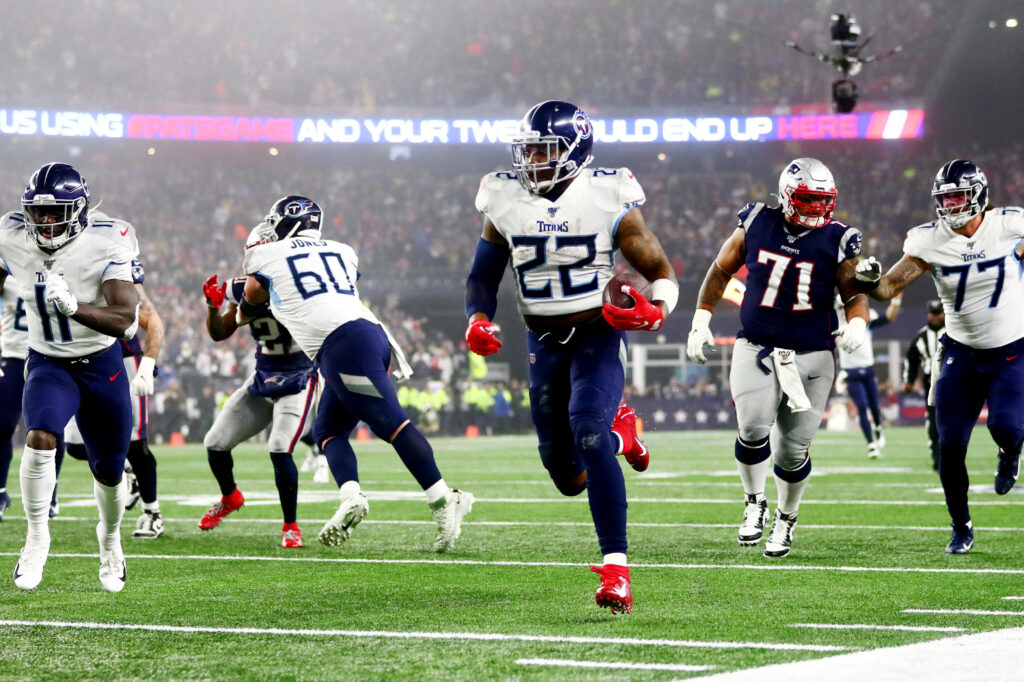Derrick Henry in Tennessee Titans uniform powering through NFL field with vivid stadium lights background Wallpaper