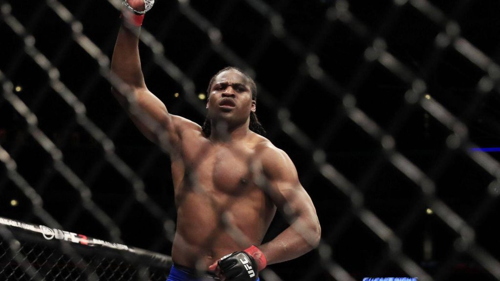 Derrick Lewis UFC heavyweight celebrating victory in Octagon with dramatic arena lighting background Wallpaper