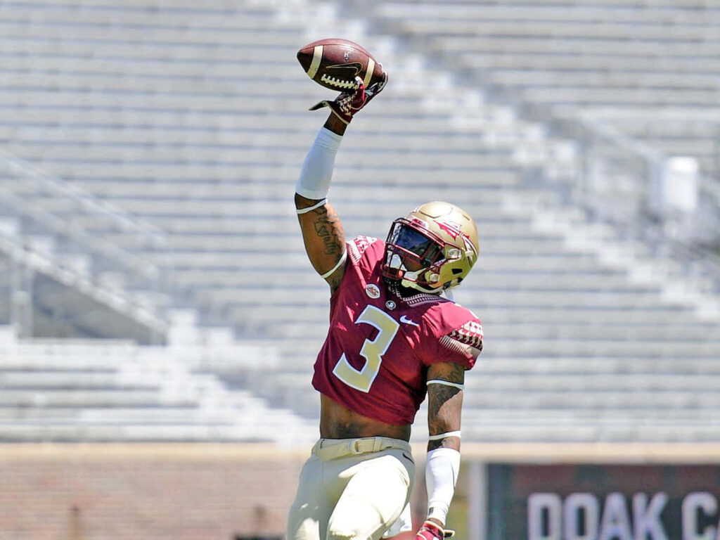 Derwin James Jr. leaping to make one-handed catch in maroon gold uniform in sunlit stadium Wallpaper