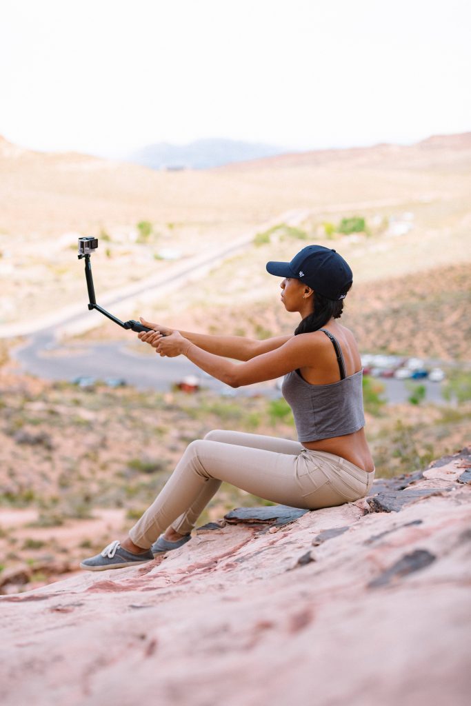 Woman in 47 cap filming desert landscape on rocky outcrop with GoPro travel adventure wallpaper