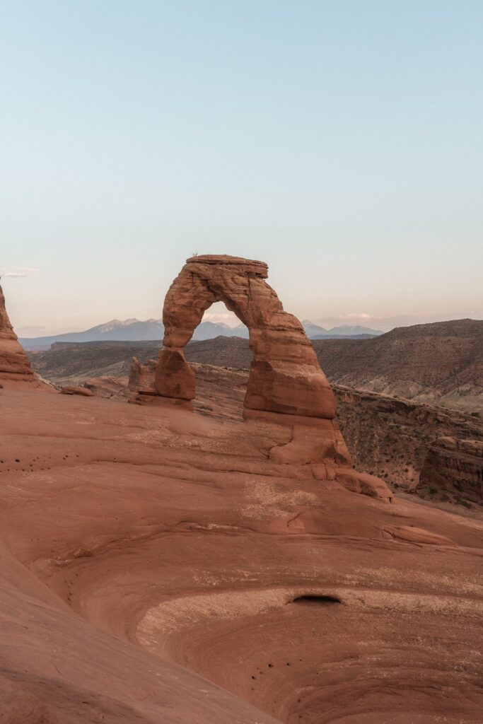 Natural arch over rugged rocks in desert canyon with distant mountains and clear blue sky wallpaper