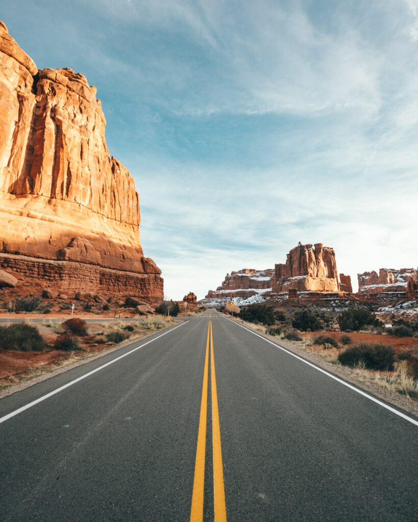 Straight asphalt road through red rock canyon with desert plants under blue cloudy sky wallpaper