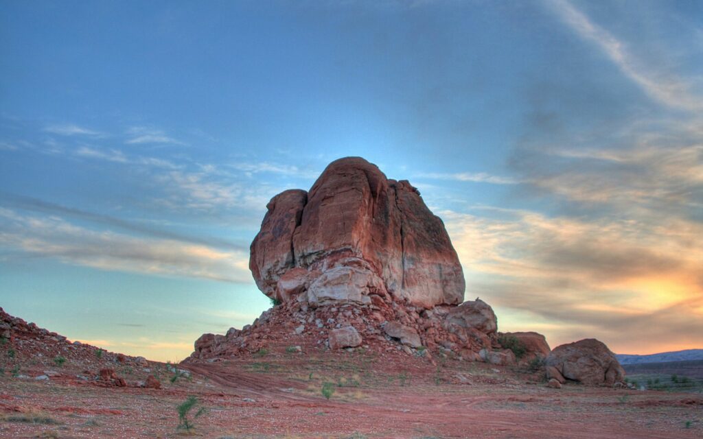 Massive rock formation in desert canyon with mountains under warm evening sky wallpaper background