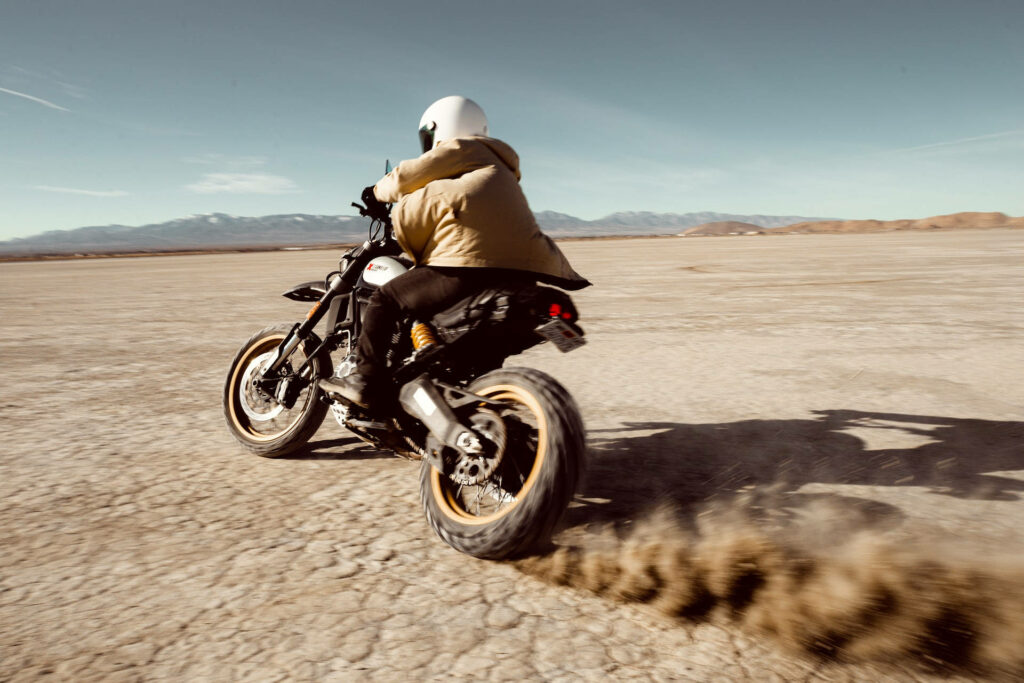 Dirt bike rider speeding across sunlit cracked desert kicking up dust off-road adventure background Wallpaper