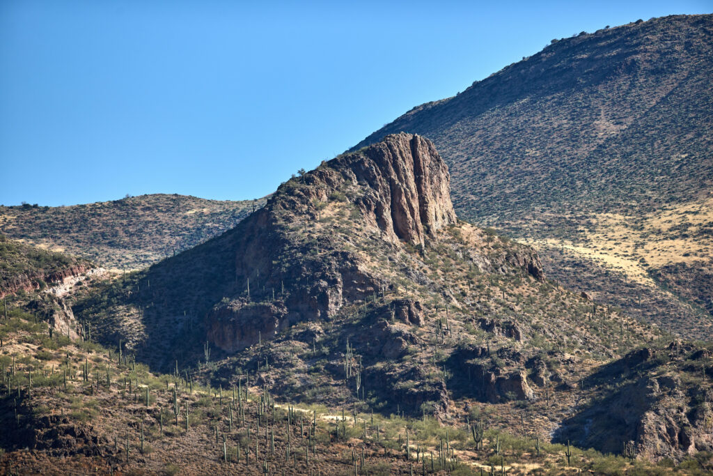 Desert landscape with rugged rocks tall cactus plants sloping mountains and clear blue sky Wallpaper
