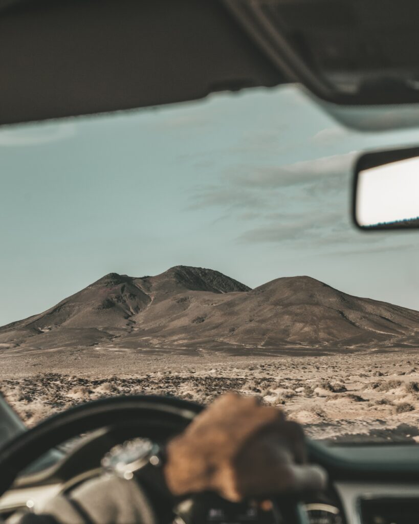First-person view of rugged desert mountains and hills under clear sky from inside a car Wallpaper