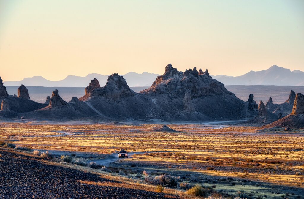 Solitary car driving on winding desert road with rugged rocks under golden sky adventure wallpaper