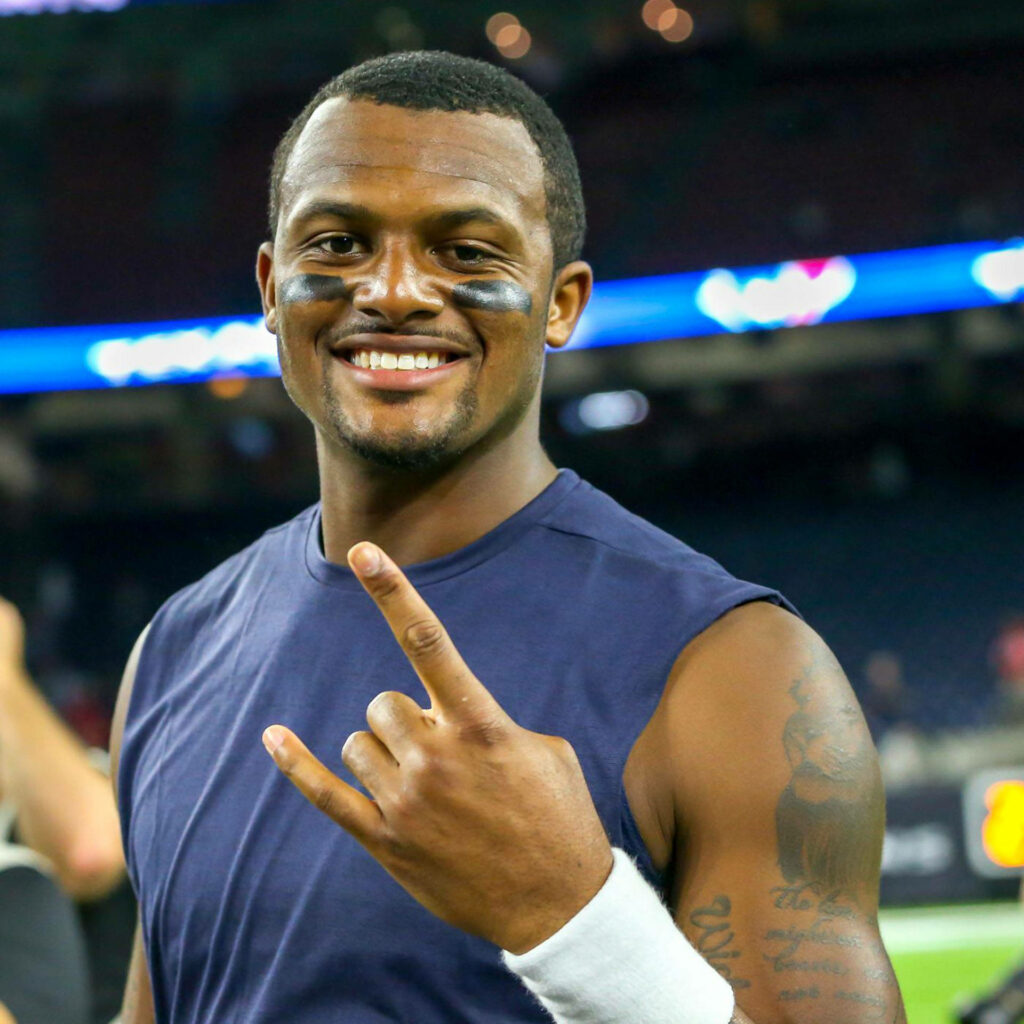 Deshaun Watson smiling confidently on field showing rock n roll sign with stadium lights background Wallpaper