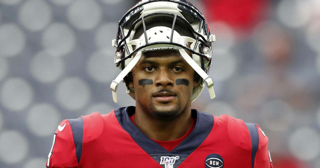 Deshaun Watson in red Houston Texans jersey warming up with blurred stadium lights background Wallpaper