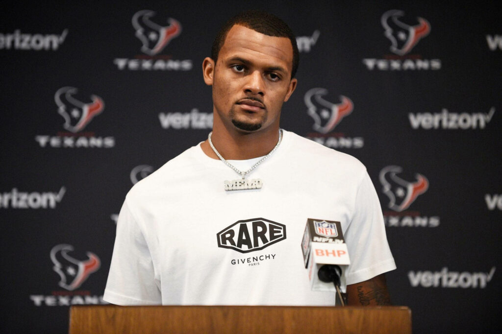 Deshaun Watson in white Givenchy tee and chain at Texans press conference with Verizon logos Wallpaper