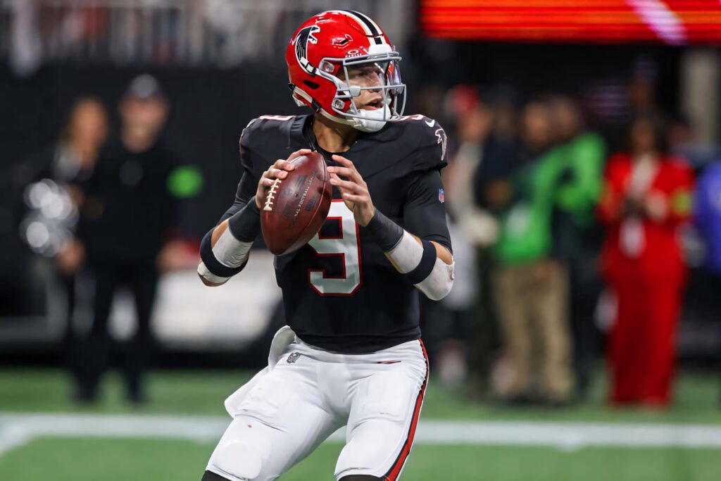 Desmond Ridder in Atlanta Falcons uniform poised as quarterback on field with stadium background Wallpaper