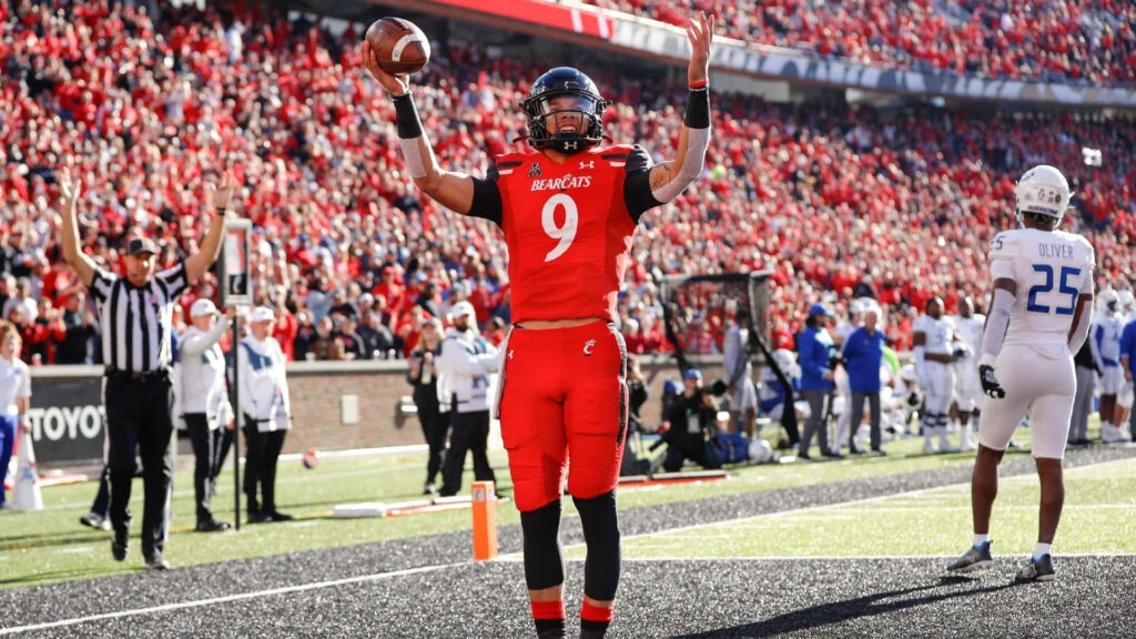 Desmond Ridder in red Cincinnati Bearcats uniform celebrates touchdown with crowd background Wallpaper