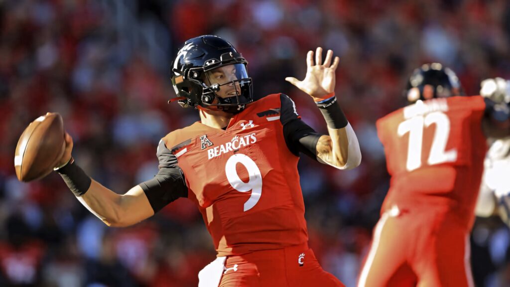 Desmond Ridder Cincinnati Bearcats quarterback mid-throw vibrant red black uniform football action Wallpaper