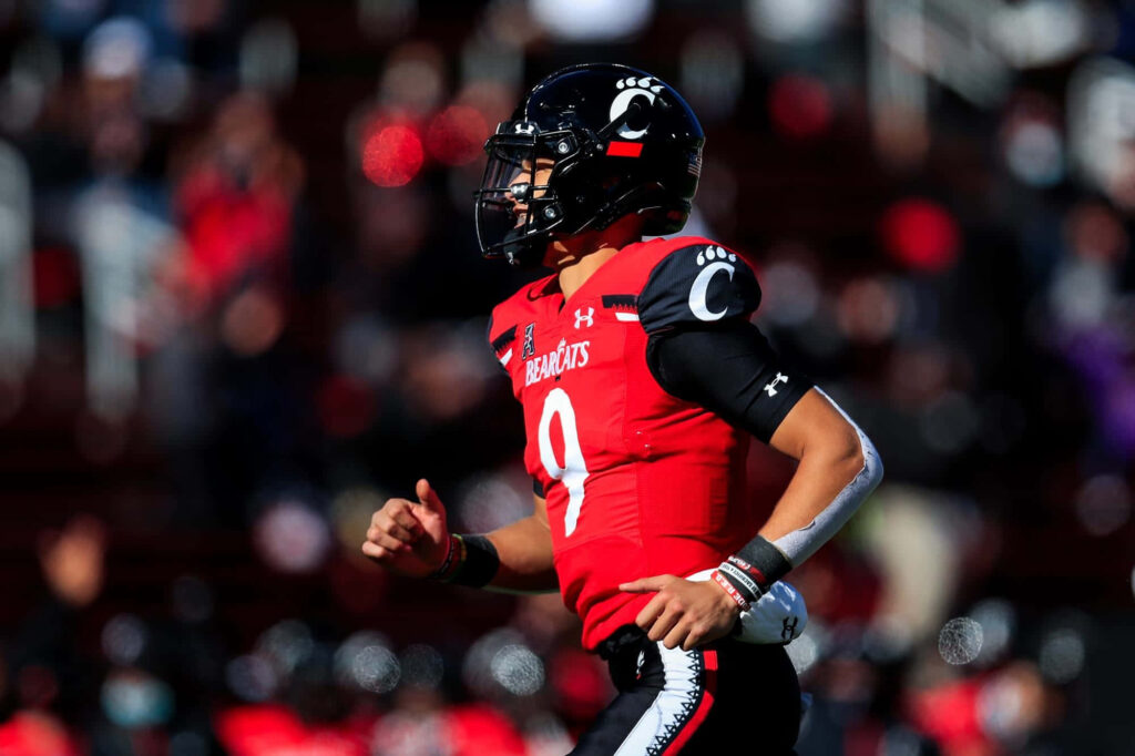 Desmond Ridder Cincinnati Bearcats quarterback in red black uniform mid-action football field Wallpaper