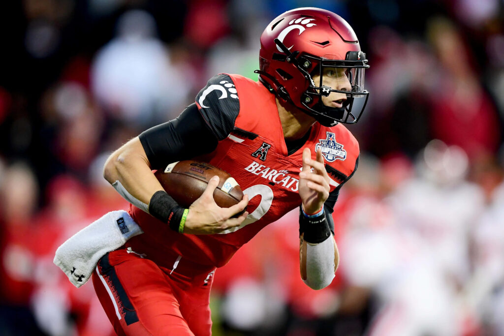 Desmond Ridder Cincinnati Bearcats quarterback in red and black uniform mid-action stadium backdrop Wallpaper