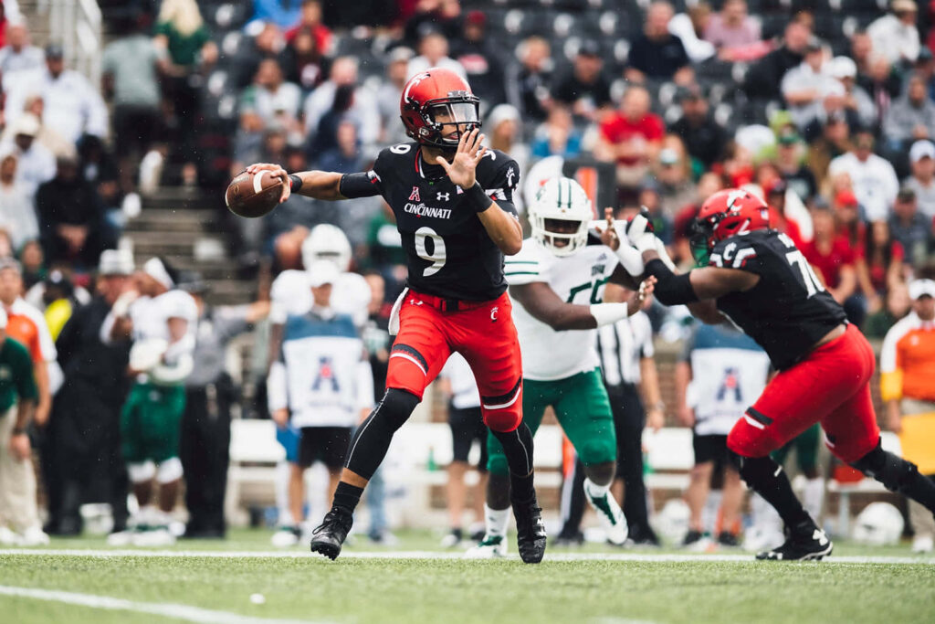 Desmond Ridder Cincinnati quarterback throwing football on vibrant field in red and black uniform Wallpaper