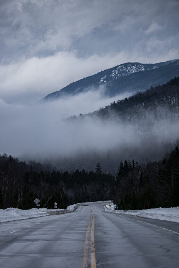 Desolate winding road with yellow lines through snowy winter landscape foggy hills and bare trees Wallpaper