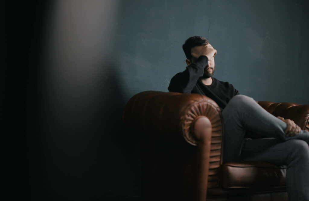 Melancholic bearded man in black sweater sitting thoughtfully in vintage leather armchair dark background Wallpaper