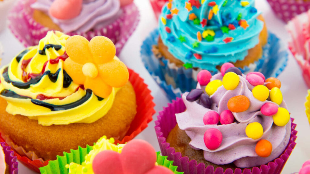 Dreamy Delights: Confectionery Creation in Vibrant Cupcake Wrappers on White Background Wallpaper