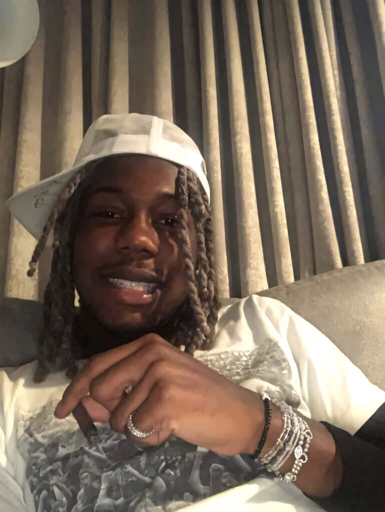 Destroy Lonely relaxing on couch wearing white mesh cap graphic tee layered jewelry cozy vibe Wallpaper