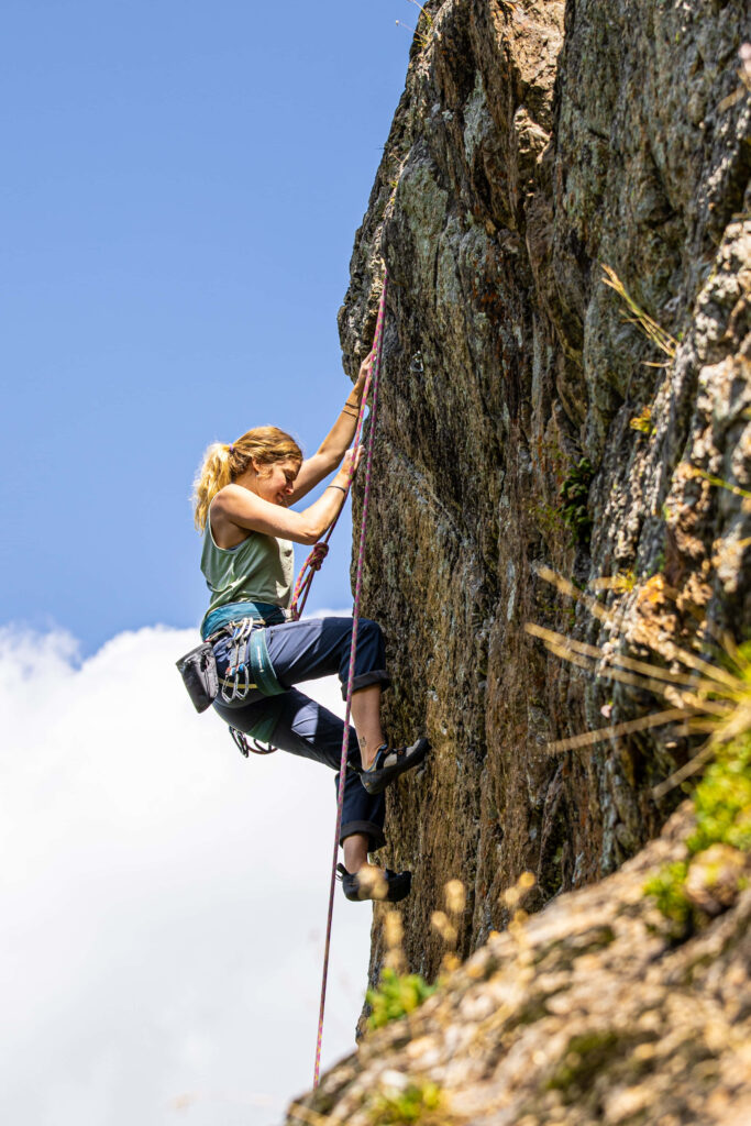 Determined climber ascending rugged rock face under bright blue sky symbolizing perseverance Wallpaper