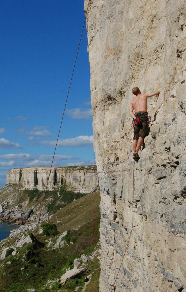 Determined climber scaling rugged limestone cliff in Portland coastal landscape sports climbing coaching Wallpaper