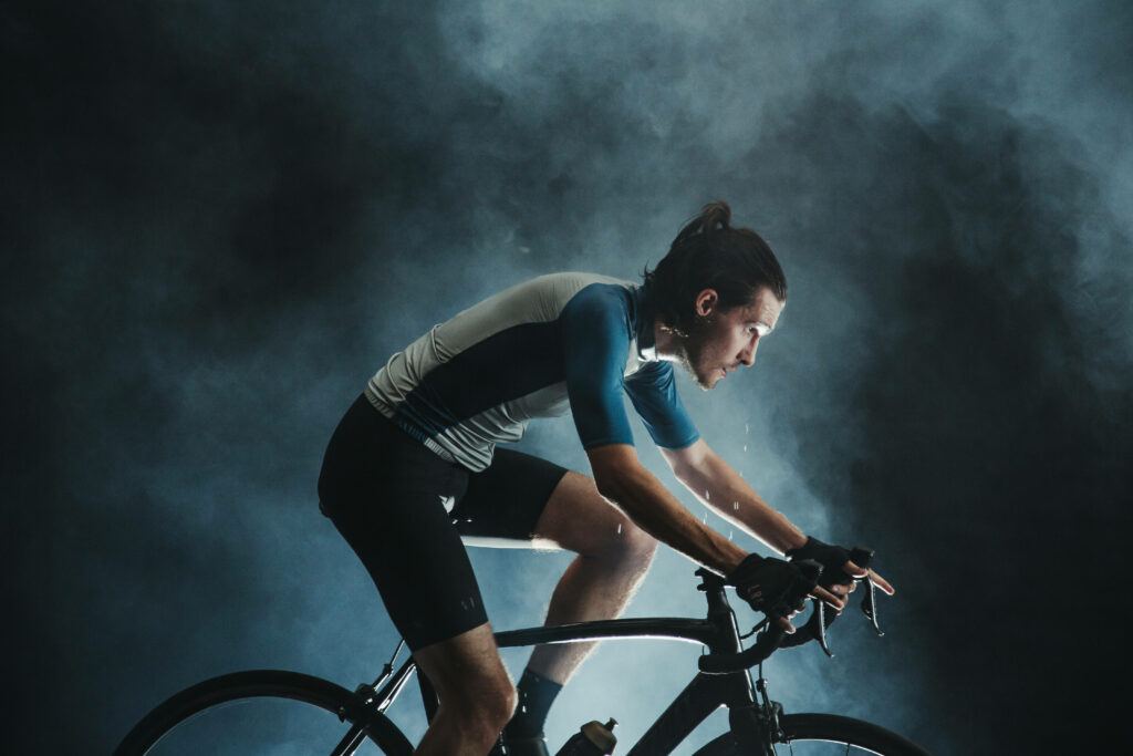 Focused cyclist on road bike in misty landscape with dramatic lighting and blue tones background Wallpaper