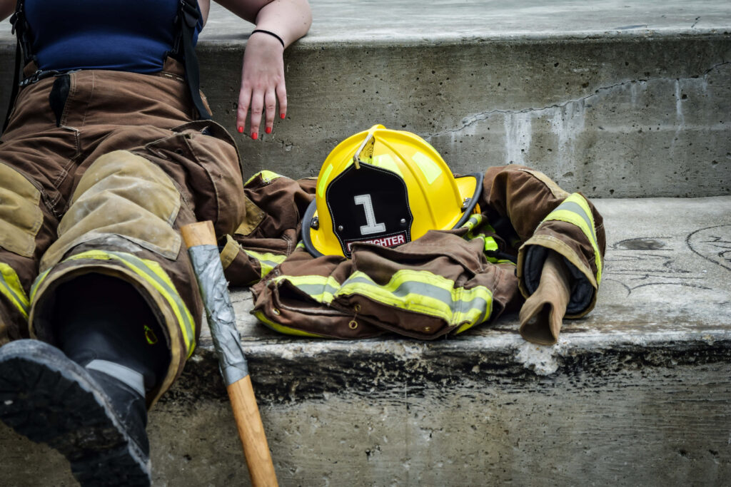 Determined female firefighter in full gear resting on steps beside yellow helmet and jacket wallpaper