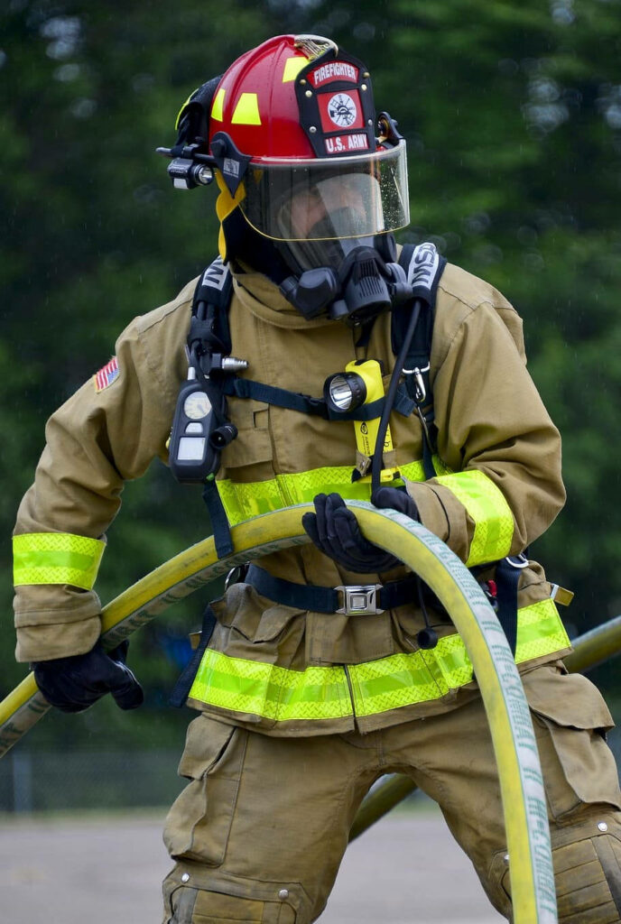 Determined firefighter in full gear using powerful fire hose outdoors ready for emergency response Wallpaper