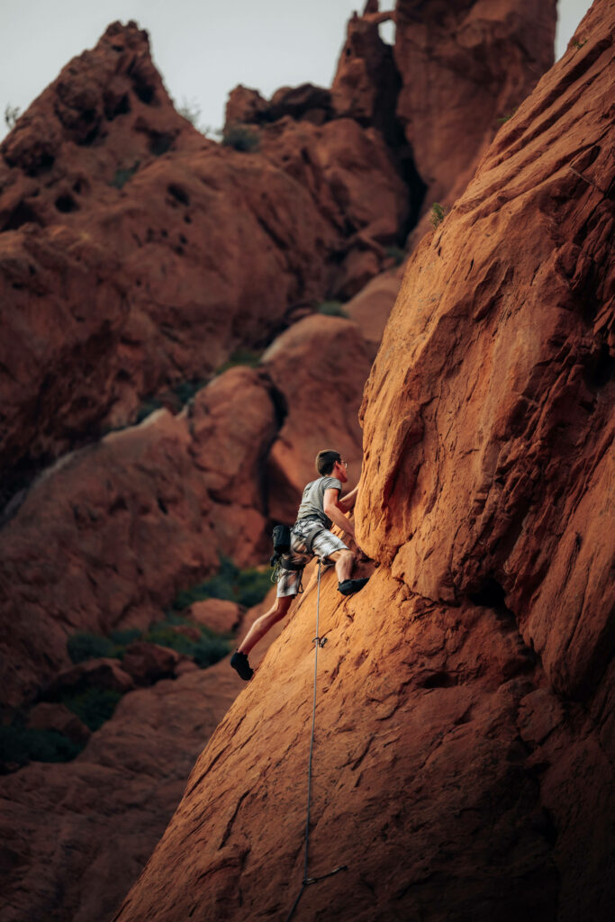 Determined man rock climbing steep rugged red rock face outdoor sport intense adventure background Wallpaper