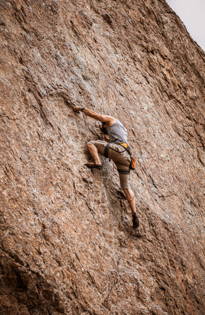 Determined man free climbing steep rock face showcasing intense challenge and thrill wallpaper