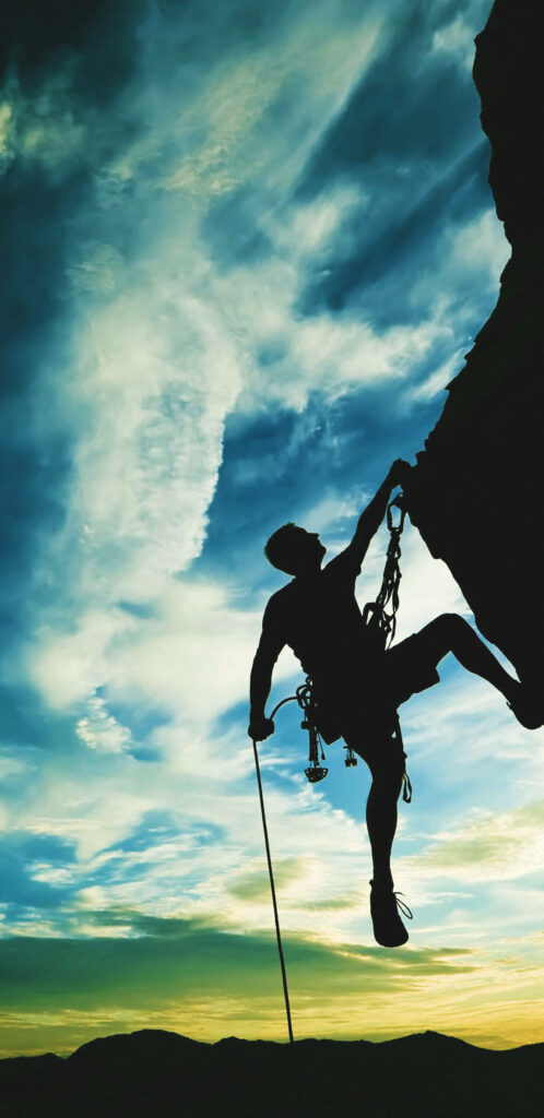 Determined rock climber scaling steep cliff under dramatic sky showcasing hustle and hard work Wallpaper